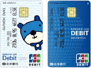 北洋銀行の、デザインの違う2種類のJCBデビットカードの写真。左のカードは、イメージキャラクター「ほっくー」が描かれた白いカード。右のカードは、イラストのない青いカード。
